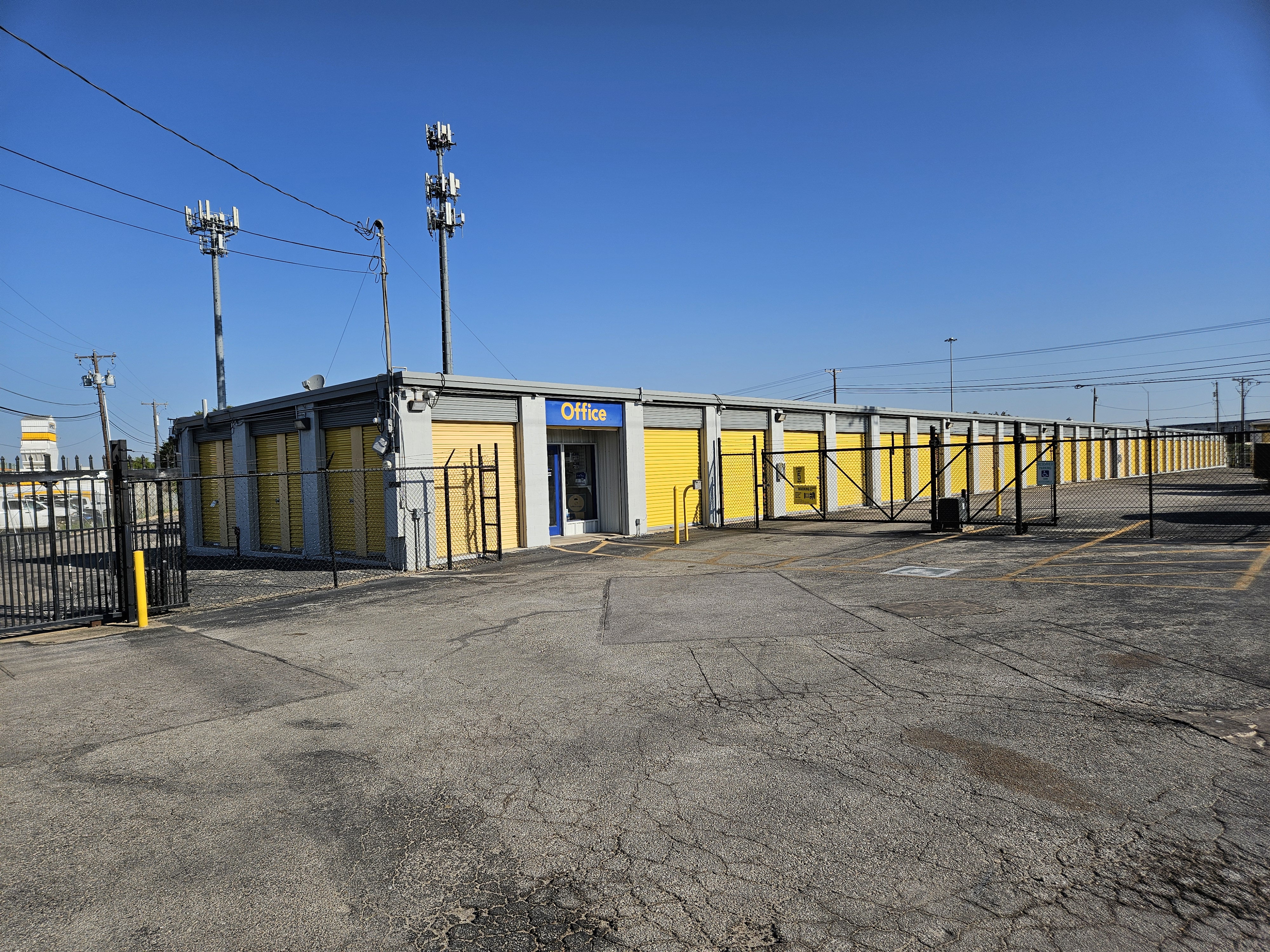 Exterior view of Round Rock Secure Storage facility with gated entry, office signage, and yellow drive-up storage units under a clear blue sky